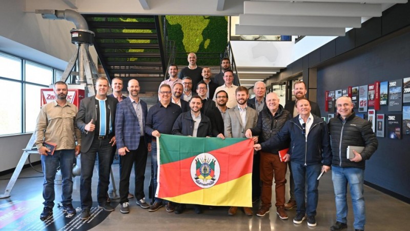 Grupo de 21 homens posa de pé para foto em frente a uma escada, segurando a bandeira do Rio Grande do Sul.