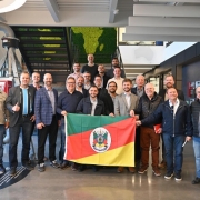 Grupo de 21 homens posa de pé para foto em frente a uma escada, segurando a bandeira do Rio Grande do Sul.