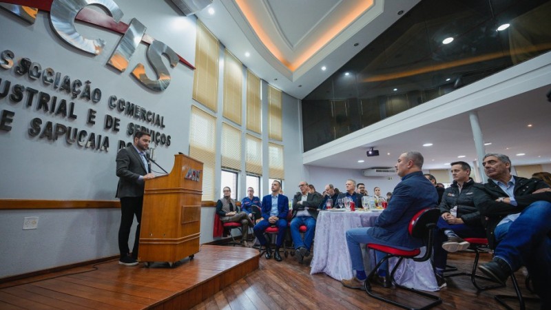 O vice-governador Gabriel Souza aparece em pé, falando ao microfone em um púlpito com o logotipo “ACIS”. À frente dele, há várias pessoas sentadas em cadeiras vermelhas, observando a apresentação.