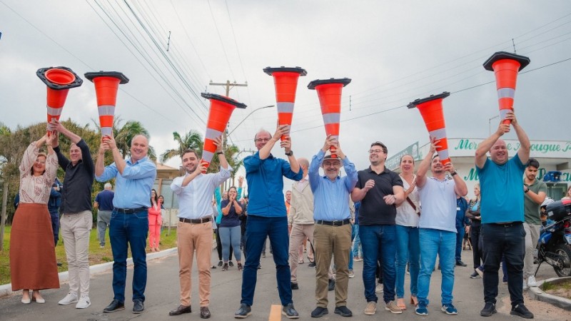 Uma foto externa de um grupo de cerca de 18 homens posando para a câmera em frente a um prédio moderno, possivelmente em um campus de pesquisa ou inovação. A maioria dos homens veste roupas casuais de negócios, como blazers, camisas polo ou casacos leves. O grupo está reunido em frente a uma placa de sinalização de metal cinza com o logotipo e o nome: "NEBRASKA INNOVATION CAMPUS" e "Greenhouse Innovation Center" em letras grandes, indicando o local da visita. O edifício ao fundo é moderno, com fachada de cor clara (cinza claro e bege) e amplas janelas horizontais escuras. O gramado em primeiro plano está verde e há uma árvore frondosa e uma luminária de rua no canto direito. O céu está nublado, e a comitiva parece estar em uma missão de pesquisa em irrigação ou tecnologia agrícola nos EUA.