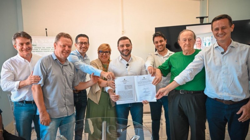 Oito pessoas posam para a foto, segurando o conv&ecirc;nio assinado. O vice-governador aparece no centro da imagem.