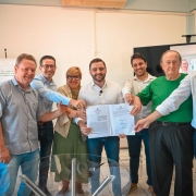 Oito pessoas posam para a foto, segurando o conv&ecirc;nio assinado. O vice-governador aparece no centro da imagem.