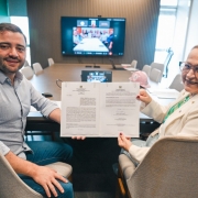 Vice governador Gabriel Souza aparece na foto ao lado da secret&aacute;ria Arita Bergmann, ambos seguram um documento, com uma tela com outros participantes online ao fundo.