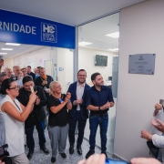 Foto horizontal mostra um grupo de cerca de 20 pessoas reunidas em um corredor iluminado de um hospital, diante da entrada de uma &aacute;rea identificada por uma placa azul no alto com o texto &ldquo;MATERNIDADE &ndash; HC Hospital de Cl&iacute;nicas&rdquo;. Entre elas, v&ecirc;-se o vice-governador Gabriel Souza e a secret&aacute;ria estadual da Sa&uacute;de, Arita Bergmann, &Agrave; direita da imagem, h&aacute; uma placa inaugural prateada fixada &agrave; parede. As pessoas est&atilde;o posicionadas em semic&iacute;rculo, olhando para a placa. Algumas est&atilde;o com c&acirc;meras ou celulares levantados, outras batendo palmas. V&aacute;rias usam crach&aacute;s ou adesivos no peito. O local tem piso claro e paredes brancas, com portas de vidro e salas iluminadas ao fundo.