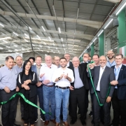 A foto registra uma cerim&ocirc;nia de inaugura&ccedil;&atilde;o em pavilh&atilde;o coberto. Um grupo grande est&aacute; alinhado segurando uma fita verde para o corte simb&oacute;lico, com o vice-governador ao centro. O local possui estandes ao fundo e ilumina&ccedil;&atilde;o t&iacute;pica de galp&atilde;o de eventos, com estrutura met&aacute;lica e corredores amplos.